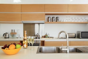 Eine moderne Küche mit Holzschränken, einer Edelstahl-Spüle und einer Arbeitsplatte mit Obstschale und Gläsern.