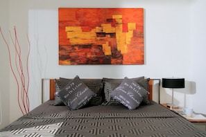 Une chambre d’hôtel comprenant un lit, des oreillers, une table de chevet, une lampe et une œuvre d’art murale.