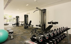 Ein Fitnessstudio mit verschiedenen Trainingsgeräten, darunter Kurzhanteln, Bänke und Kraftgeräte.