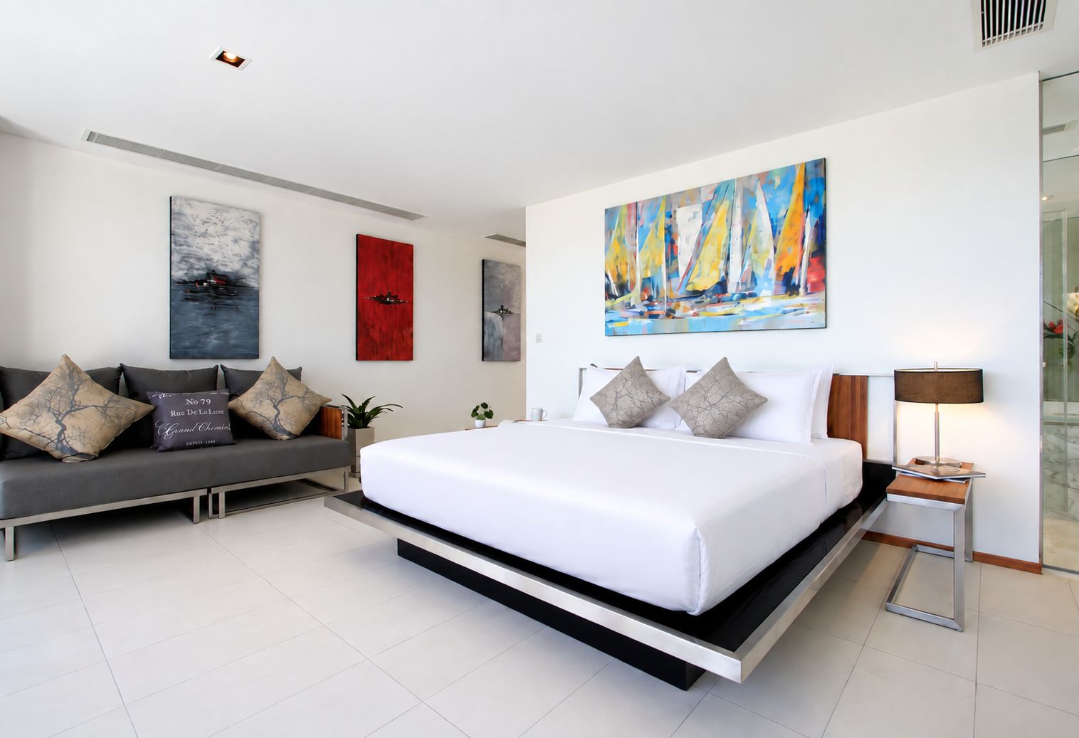 Una habitación de hotel moderna con una cama grande, un sofá y un cuadro de veleros.