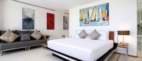 Una habitación de hotel moderna con una cama grande, un sofá y un cuadro de veleros.