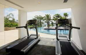 Two treadmills in a room with a large window overlooking a pool and tropical scenery.