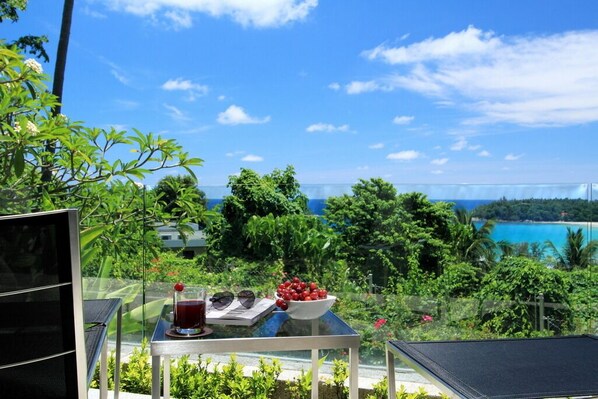 A table with a bowl of fruit and a glass of red beverage, set against a backdrop of lush greenery and a clear blue sky. - The Heights Penthouse 3bedroom A2 near Kata Beach (Karon)