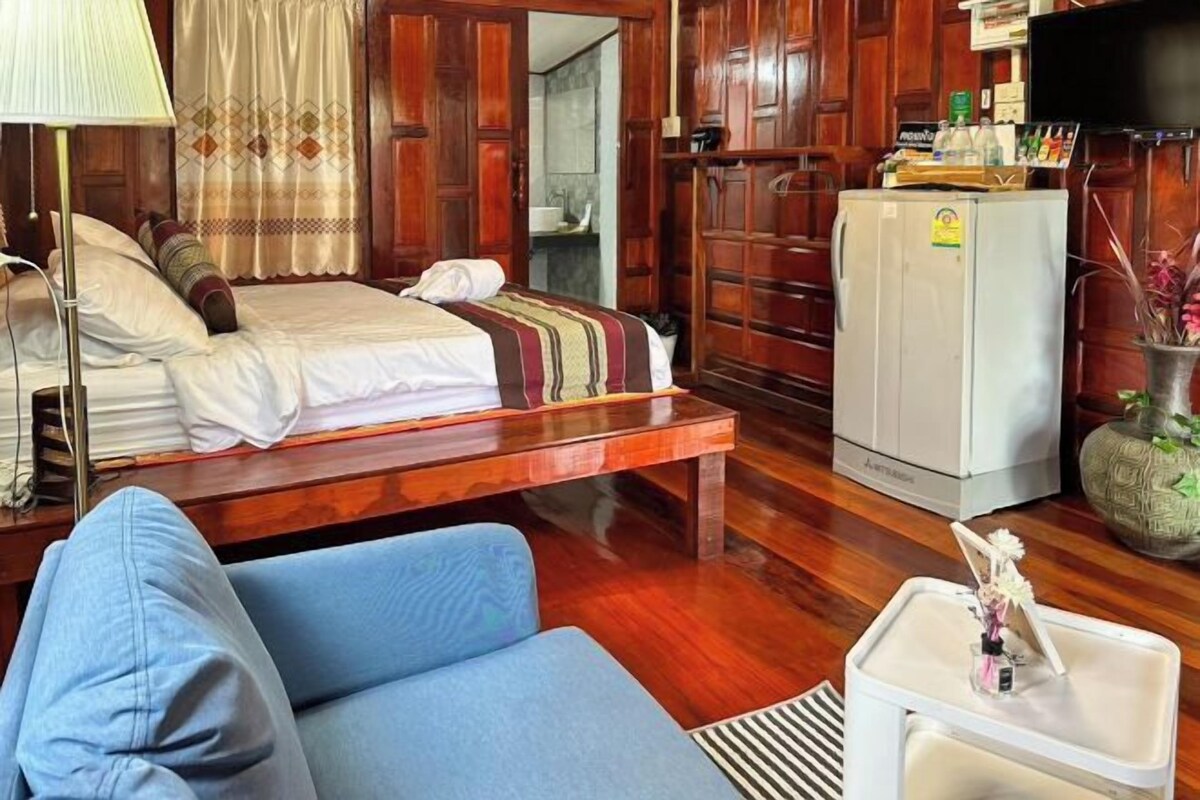 A room with a bed, a sofa, a small table, a refrigerator, and wooden paneling.