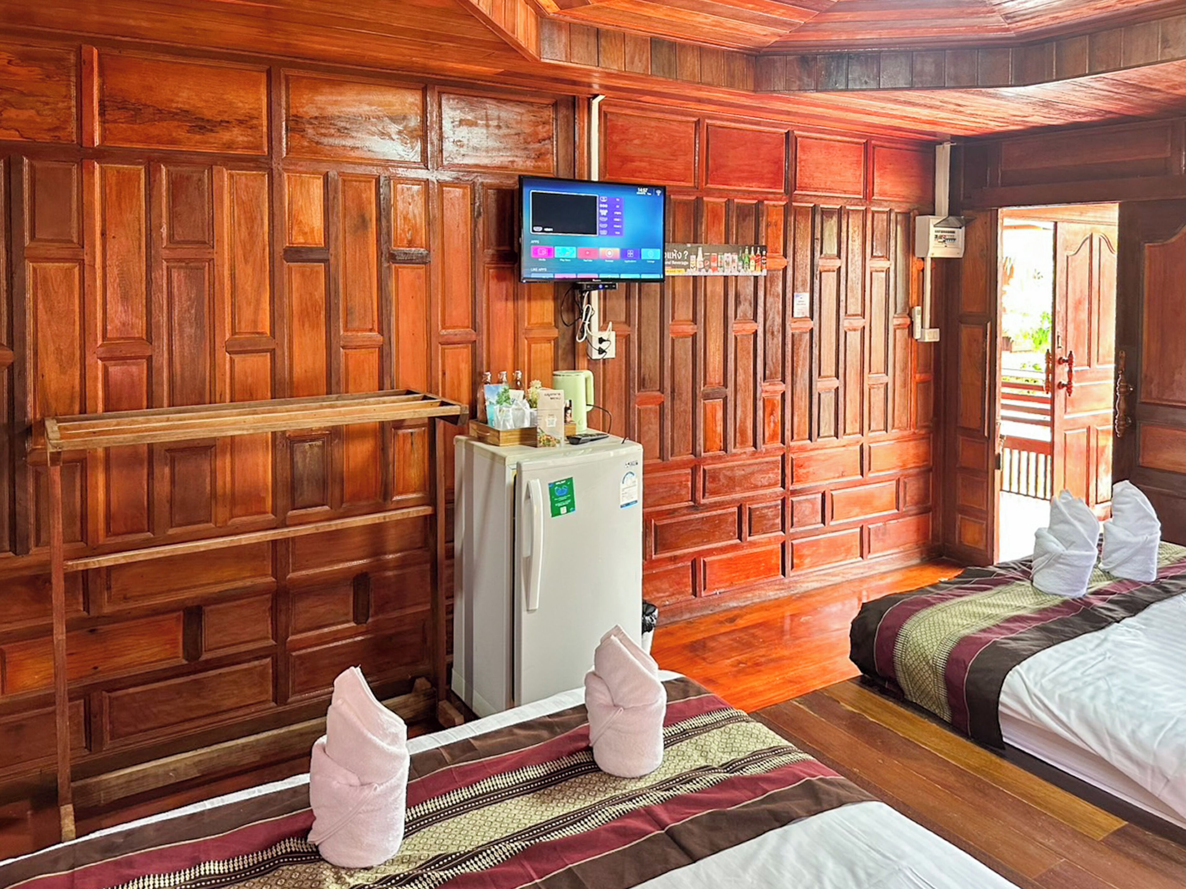 Una habitación con paneles de madera, dos camas, un televisor en la pared y un refrigerador.