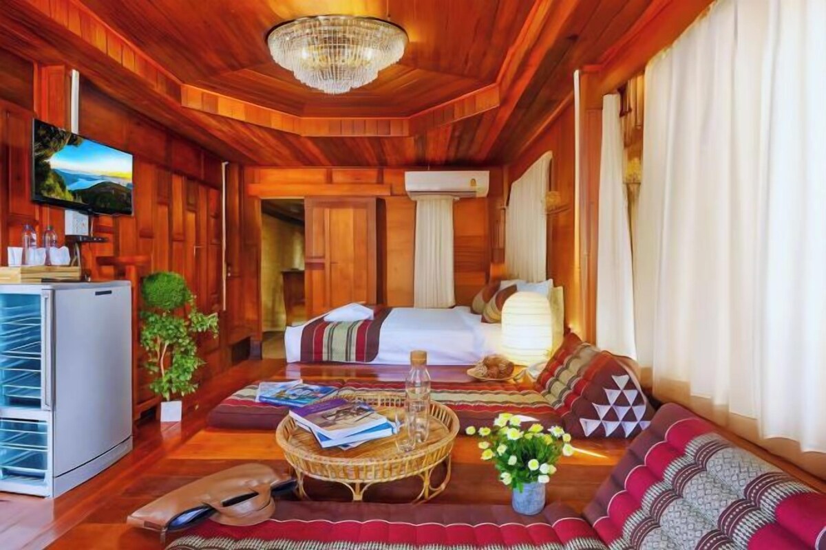 Una habitación de madera con una cama, un televisor, un refrigerador y una araña.