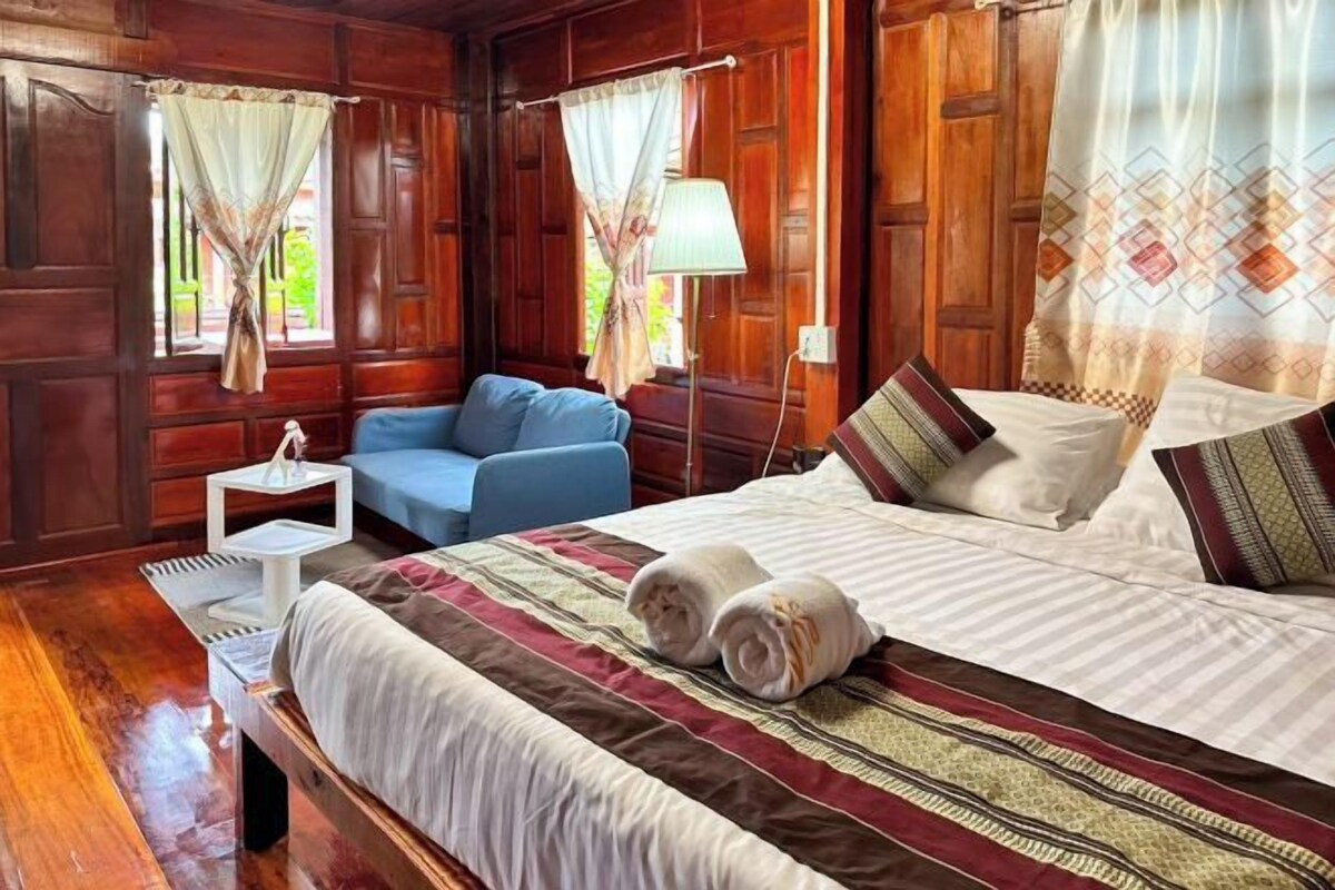 A wooden room with a bed, a small table, a chair, and a lamp.