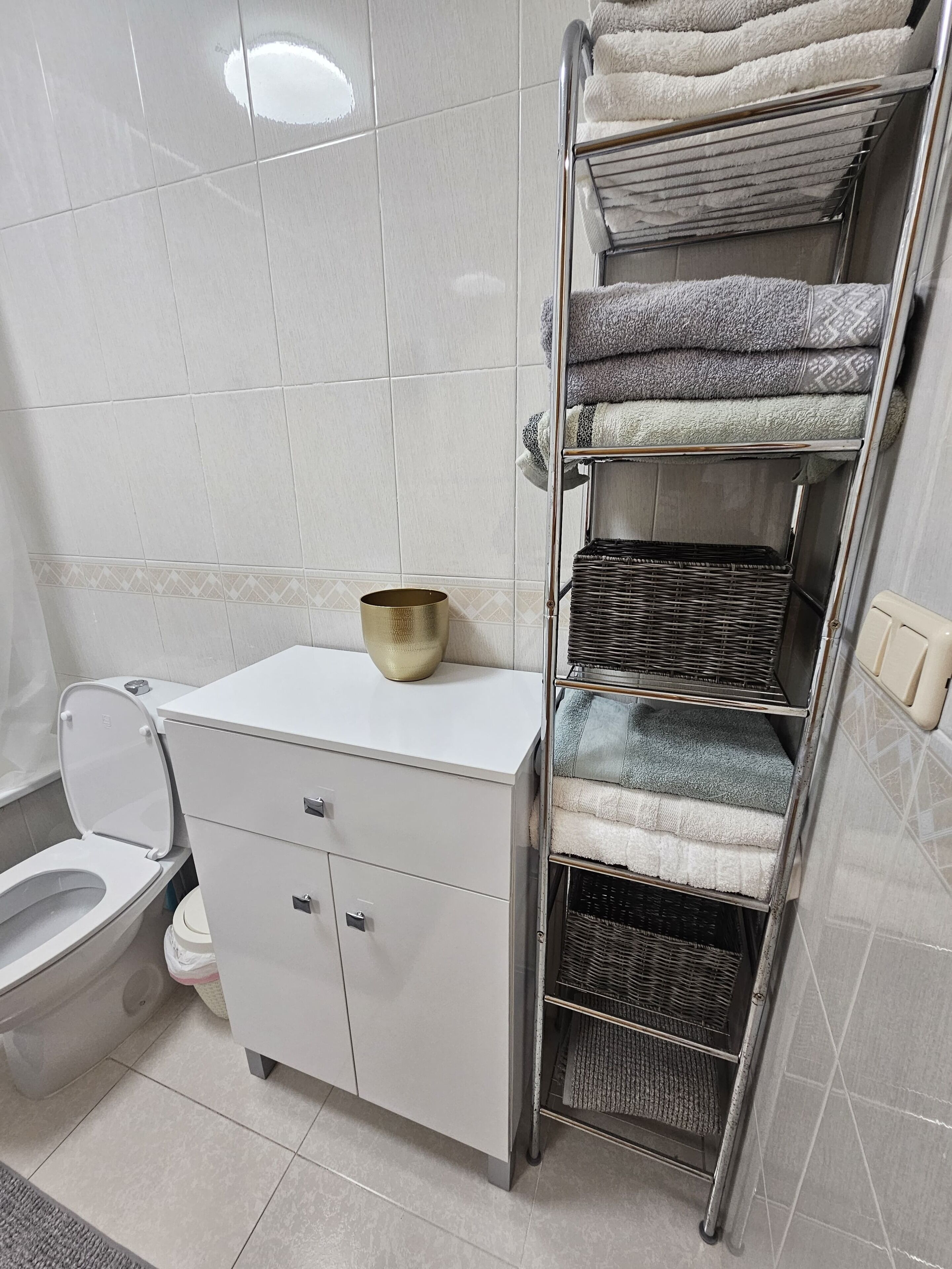 A bathroom with a toilet, a white cabinet, and a towel rack with folded towels.