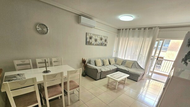 A living room with a dining area, a gray sofa, a coffee table, and a painting on the wall.