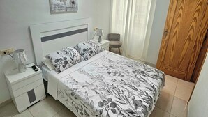 A bedroom with a bed, nightstands, a lamp, a painting, a chair, and a wooden door.