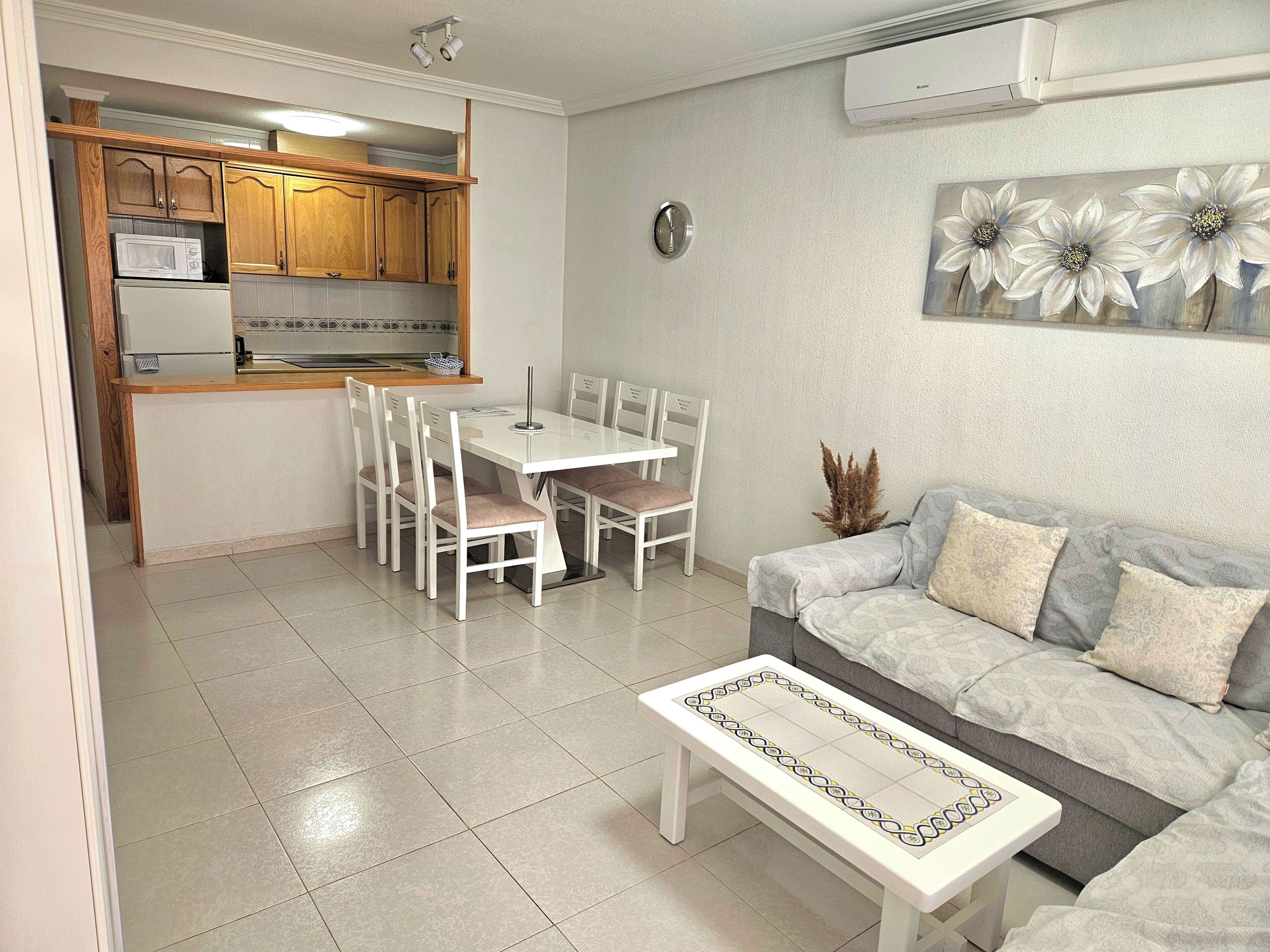 A compact living space with a dining area, kitchenette, and a sofa with patterned cushions.