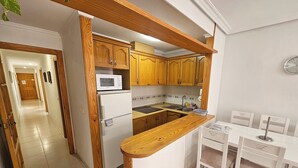 A compact kitchen with wooden cabinets, a white refrigerator, a microwave, and a sink. There is a small dining area with a table and chairs.