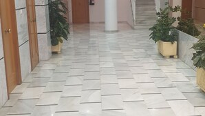 A spacious hallway with a marble floor, wooden doors, and potted plants. A staircase is visible in the background.