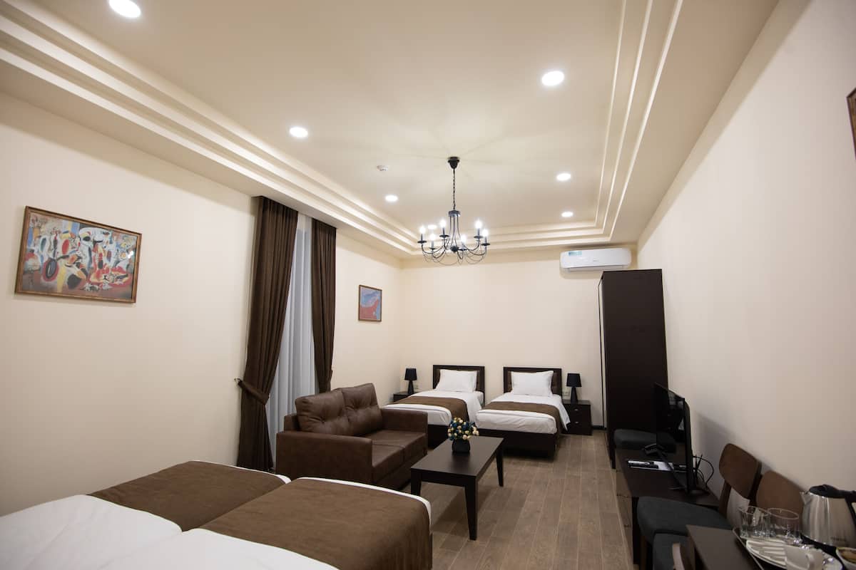 A hotel room with two beds, a sofa, a desk, and a television.