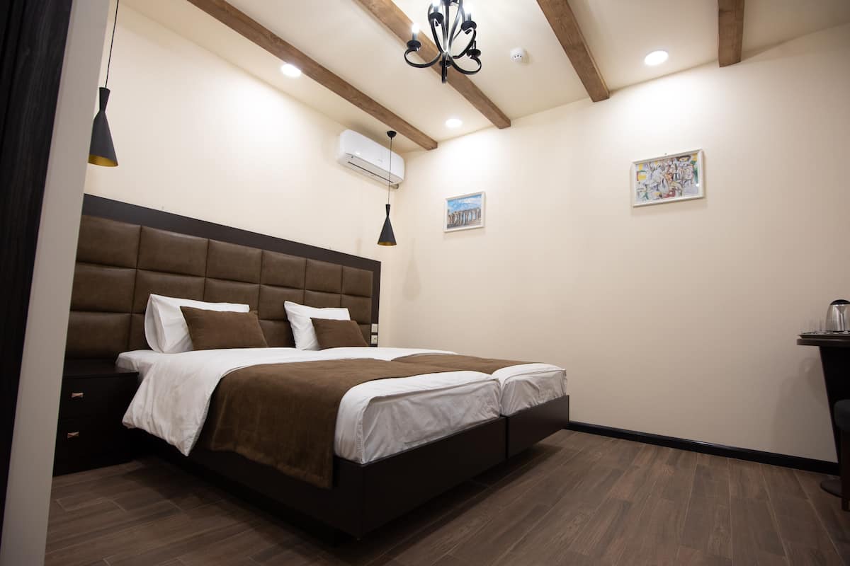 A bedroom with a large bed, wooden beams, an air conditioning unit, and a small table with a kettle.