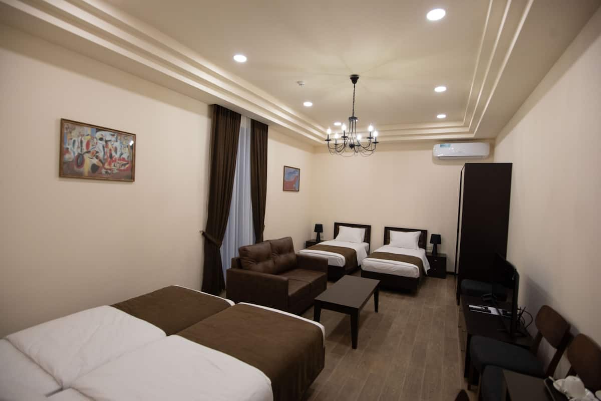 A hotel room with two beds, a sofa, a desk, a TV, and a chandelier.
