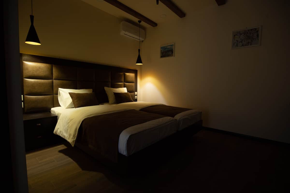A bedroom with a large bed, two bedside tables, a headboard, and a hanging light fixture.