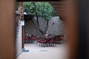 An outdoor dining area with wicker chairs and a table set for two, surrounded by a brick wall and a tree. - Boutique Living Hotel (Yerevan)