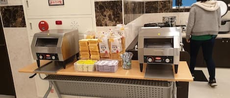 Een buffet met twee ovens, diverse verpakte maaltijden en een persoon op de achtergrond.