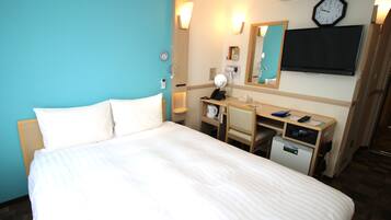Quarto de hotel com cama, escrivaninha e pequeno frigorífico.