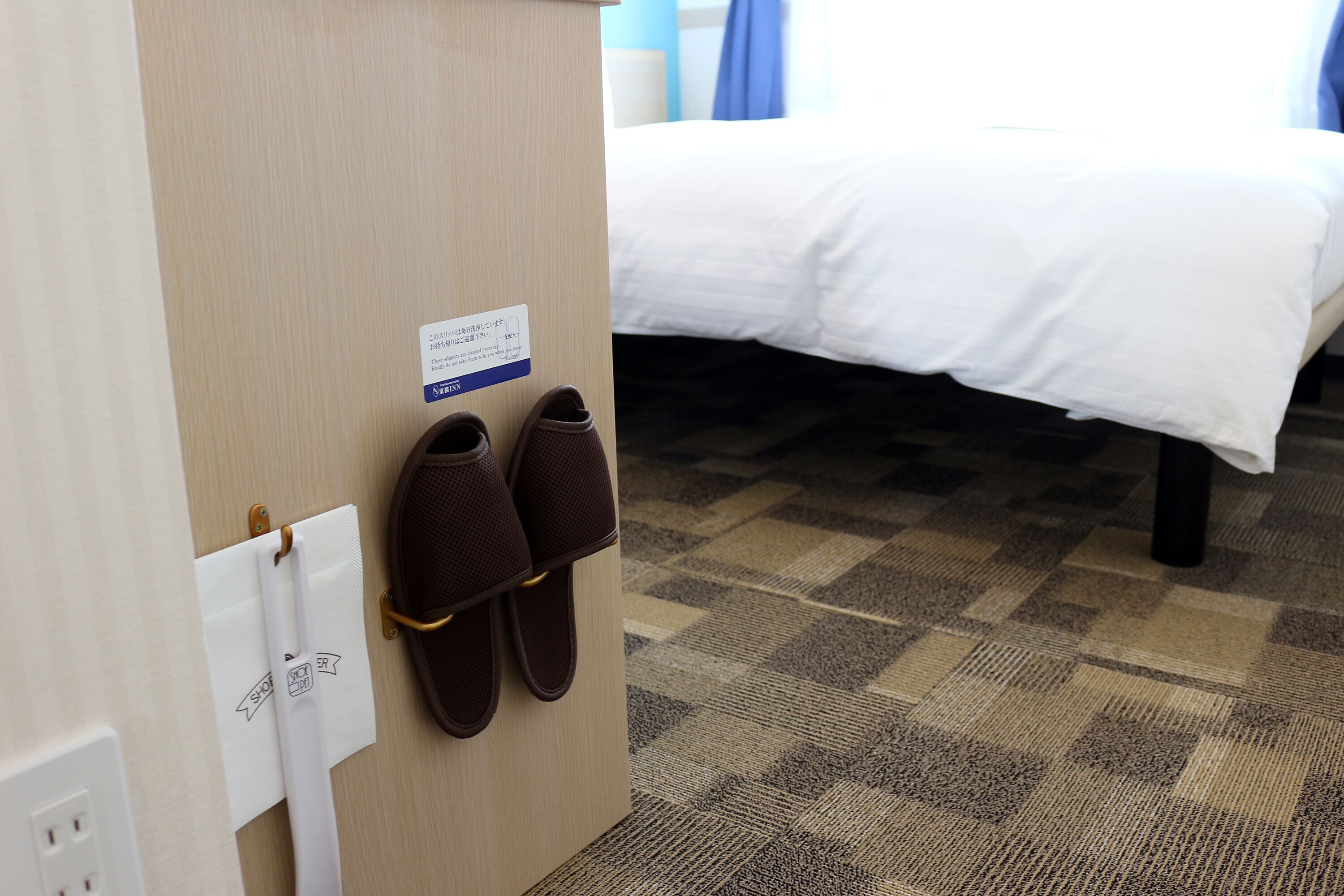 A hotel room with a bed, a pair of slippers hanging on a hook, and a sign with text.