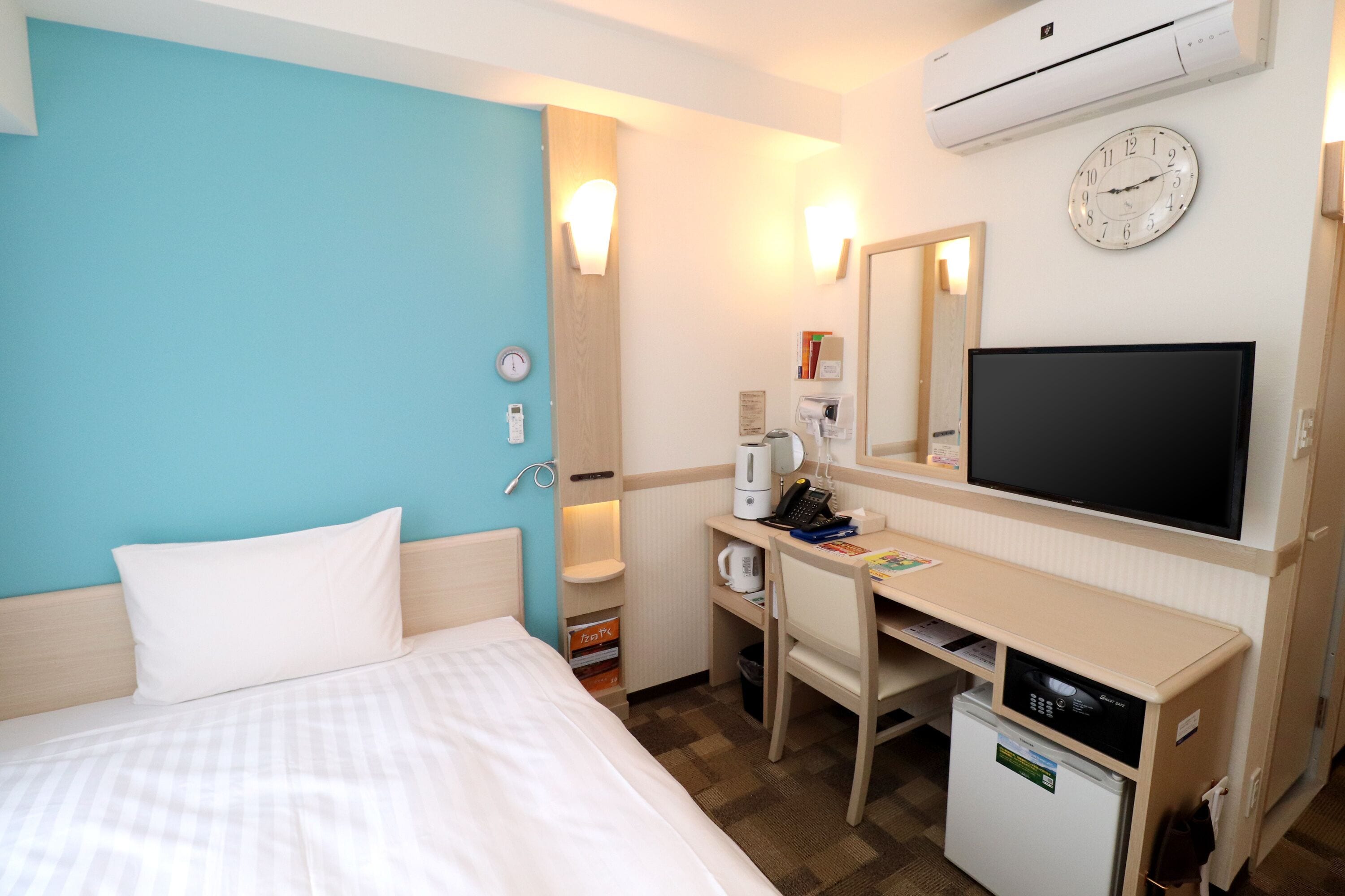 Una habitación de hotel con cama, escritorio, televisor, reloj y aire acondicionado.