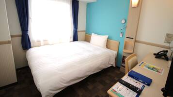 Habitación de hotel con una cama grande, un escritorio con teléfono y computadora, y una ventana con cortinas.