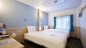Hotelkamer met twee bedden, een bureau met stoel, een klein tafeltje, een raam met gordijnen en een plafondlamp.