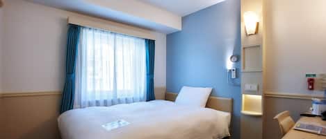A hotel room with a bed, a desk, a chair, a window with curtains, a wall-mounted light, and a clock.