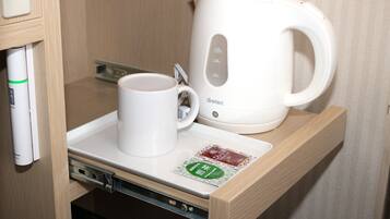 A white electric kettle and a white mug on a tray in a wooden cabinet.