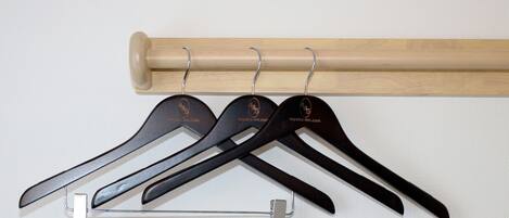 A wooden coat rack with three black hangers and a metal clip.
