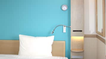 Una habitación de hotel con una cama, un termostato en la pared y una pequeña estantería con un libro.