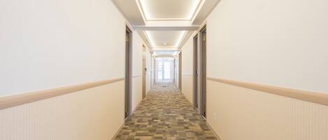 A hotel hallway with carpeted flooring, white walls, and doors on both sides.