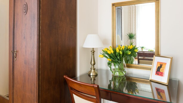 A wooden desk with a glass top, a brass lamp, a vase with yellow flowers, and a framed picture. - KrakowRentals - Belle Epoque 1 Apartment (Kraków)