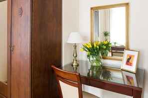 Et træskrivebord med glasplade, en messinglampe, en vase med gule blomster, et indrammet billede og et spejl med gylden ramme.