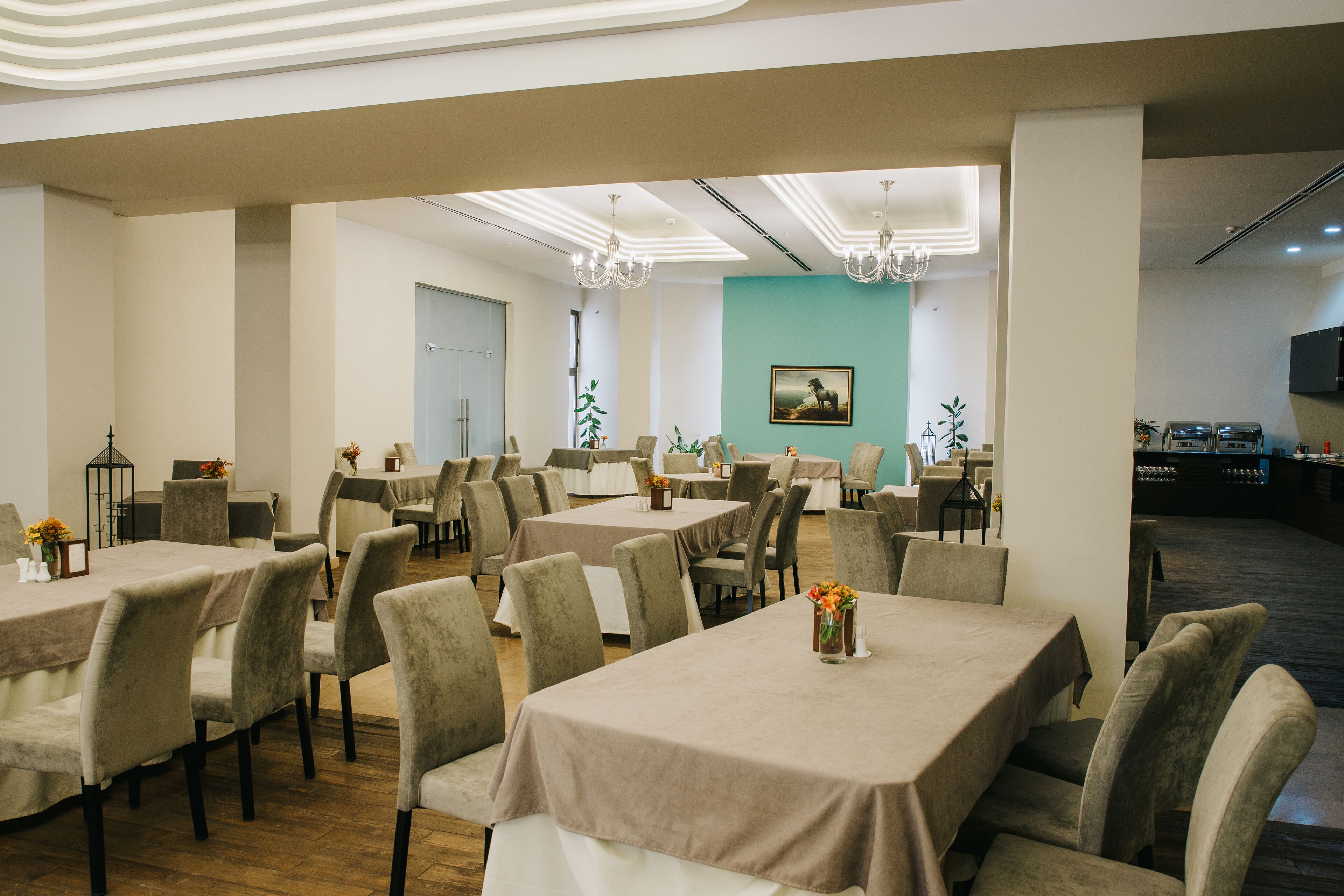 A spacious dining area with multiple tables and chairs, a teal accent wall, and a chandelier.