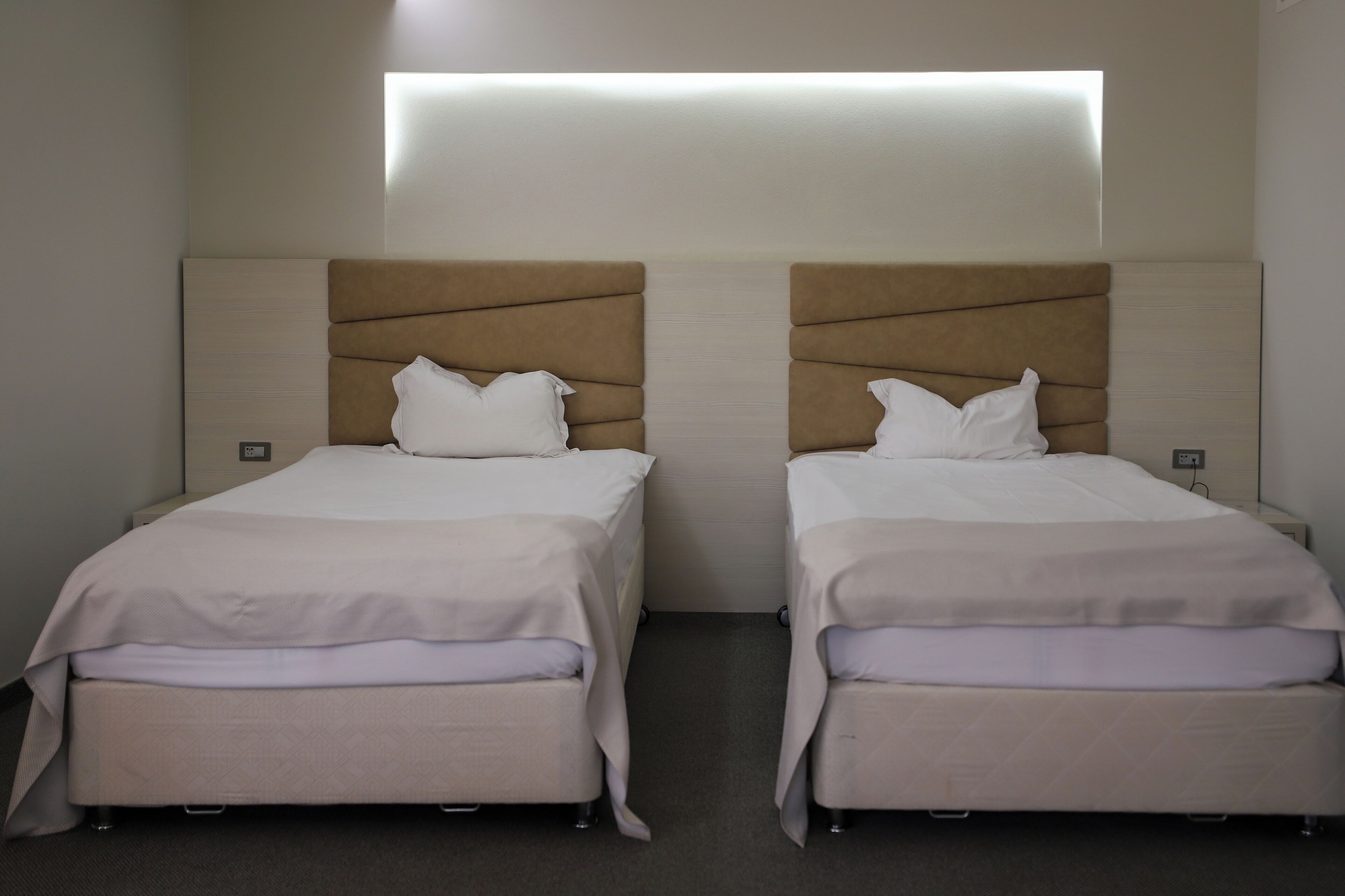 Two single beds with headboards, a neutral color scheme, and a wall-mounted light fixture.