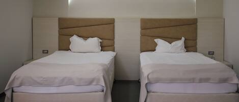 Two single beds with headboards, a neutral color scheme, and a wall-mounted light fixture.