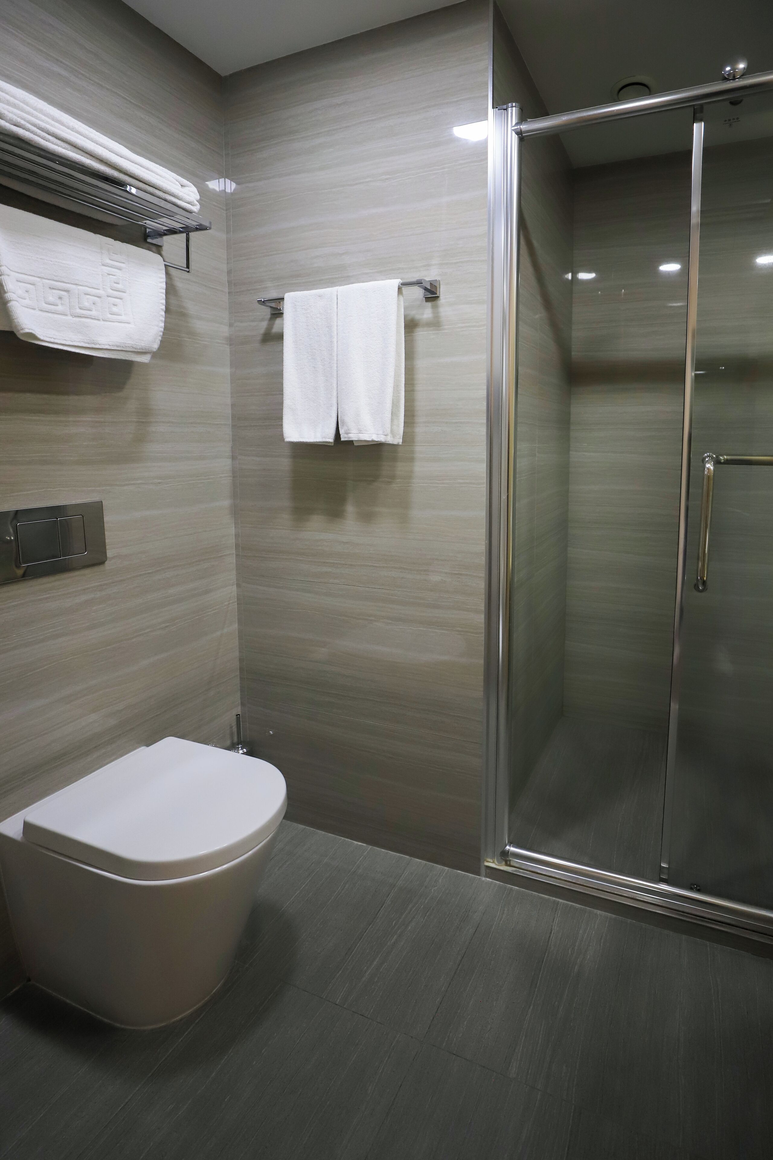 Une salle de bain moderne équipée de toilettes, d’une douche à parois de verre et d’un porte-serviettes avec deux serviettes blanches.