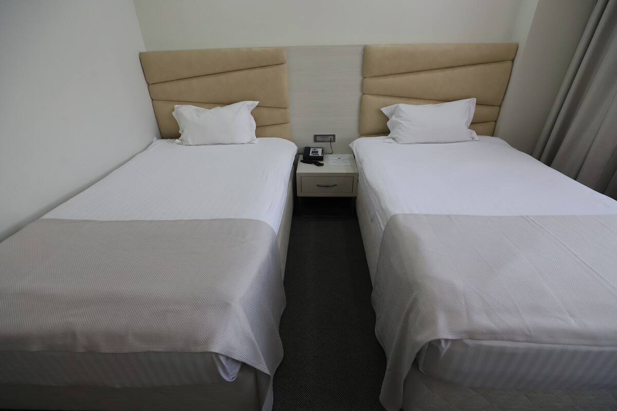 Une chambre d’hôtel avec deux lits simples, chacun doté d’une tête de lit, d’une table de chevet avec un téléphone et un bloc-notes, et d’un sol recouvert de moquette.