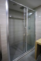 Een douche met glazen wanden en een metalen frame, een houten bankje en een betegelde vloer.
