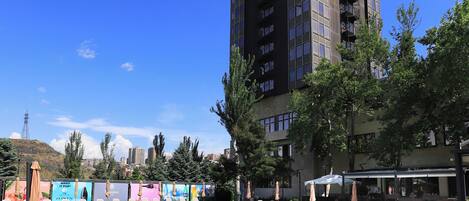 A swimming pool area with lounge chairs and umbrellas, surrounded by trees and a tall building in the background.