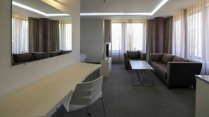 A modern hotel room with a flat-screen TV, a sofa, a desk, and a large mirror.