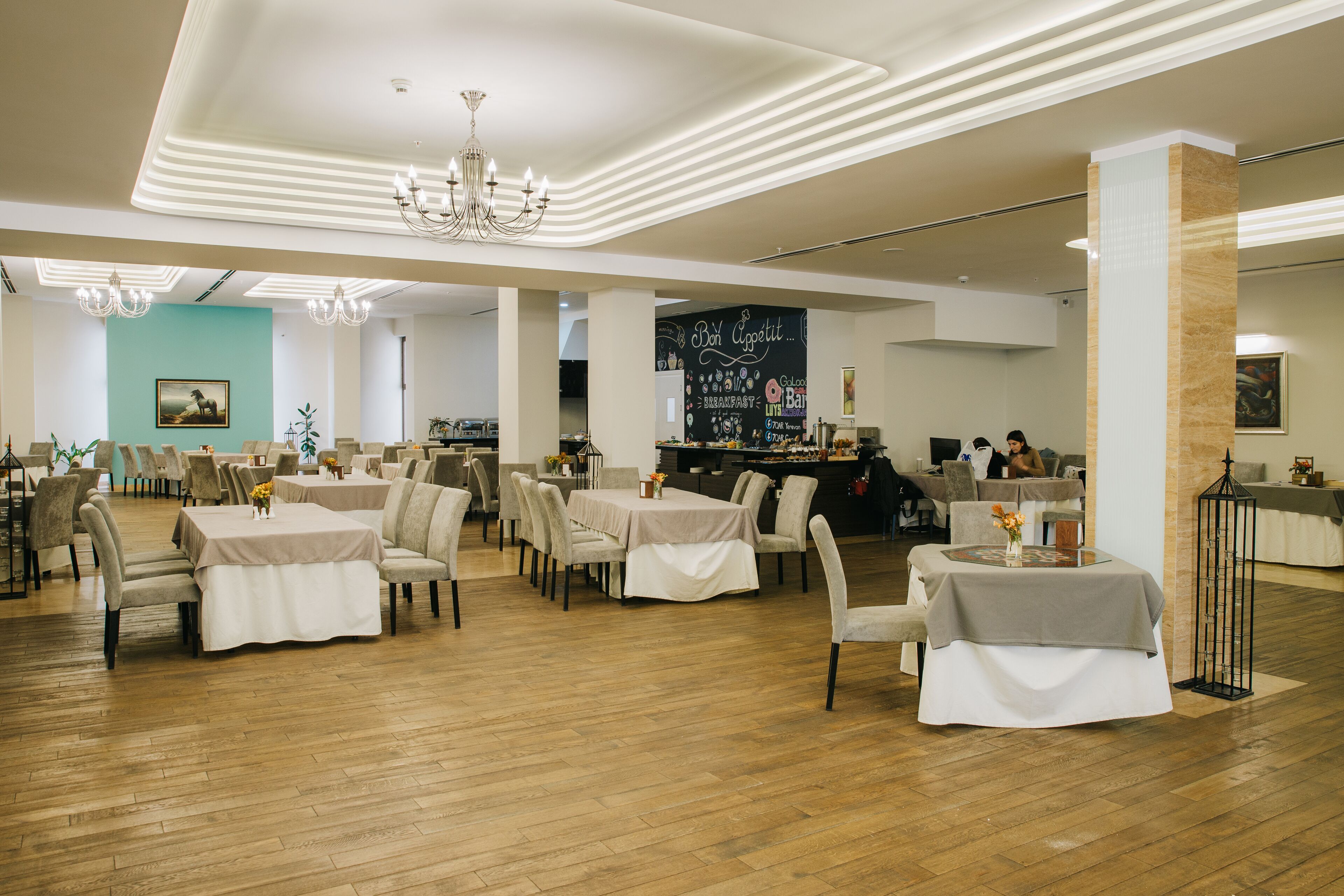 Uma ampla sala de jantar com várias mesas e cadeiras, um candelabro e um cardápio em lousa.