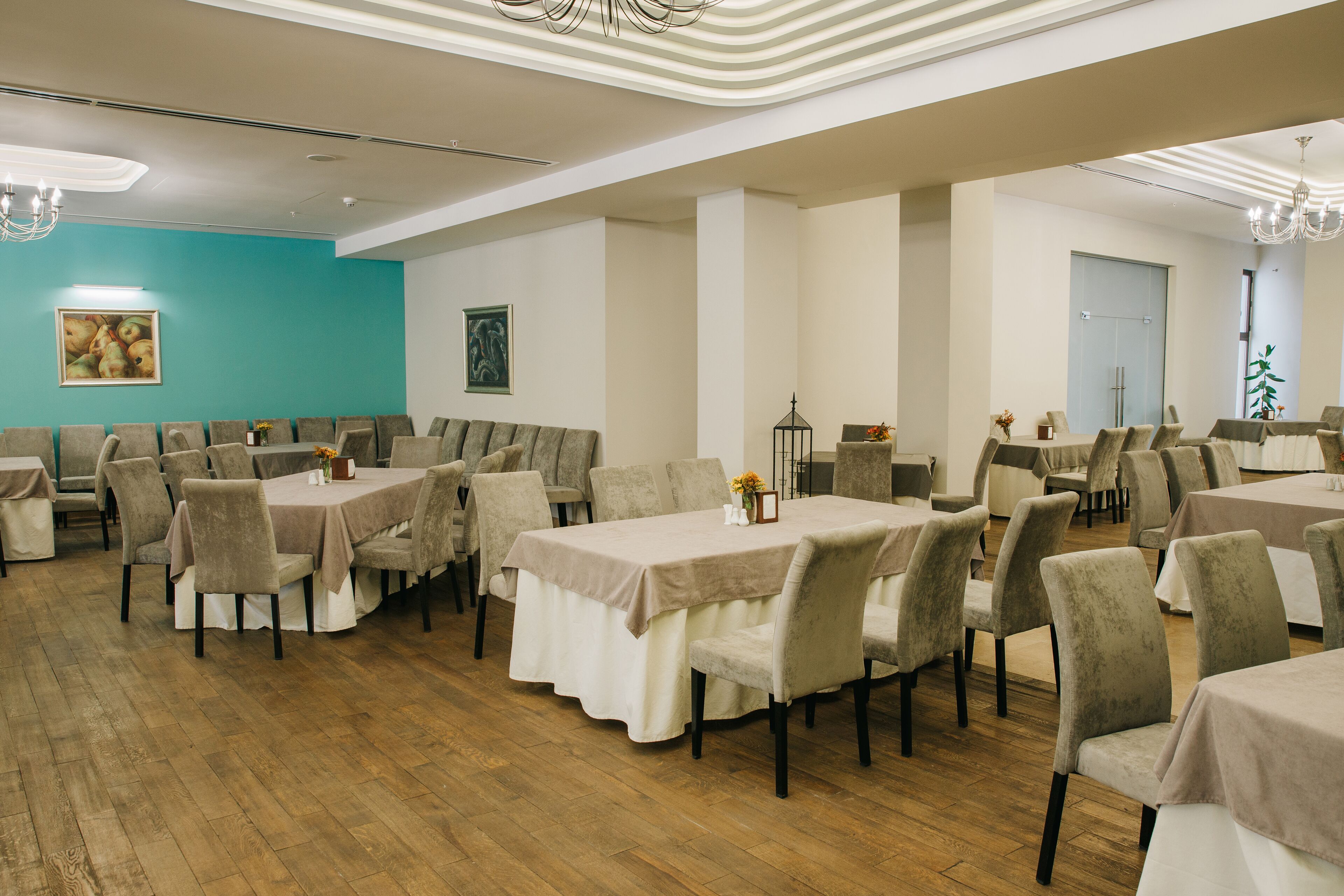 A spacious dining area with multiple tables and chairs, wooden flooring, and a teal accent wall.