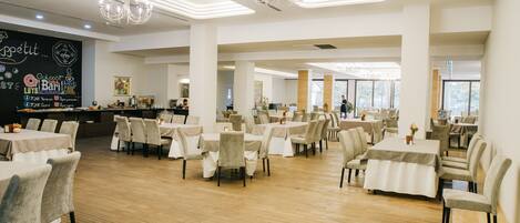 A spacious dining area with multiple tables and chairs, a chalkboard menu on the wall, and large windows allowing natural light.
