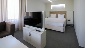 A hotel room with a bed, a TV on a stand, a bedside table, and a sofa.