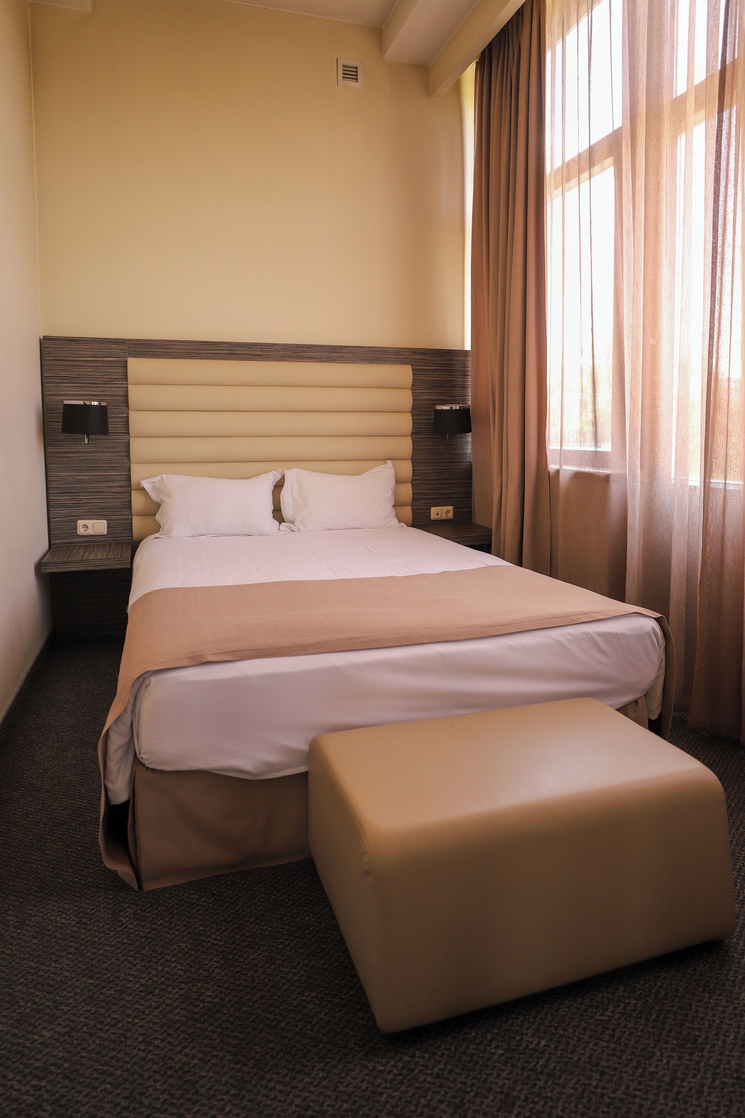 A hotel room with a large bed, a bedside table with a lamp, and a window with curtains.