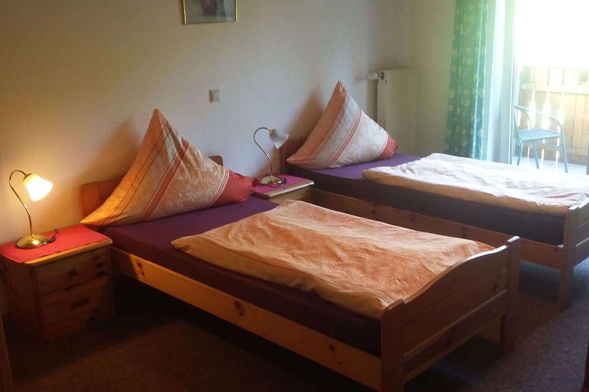 A room with two wooden beds, each with a pillow and a small bedside table with a lamp.
