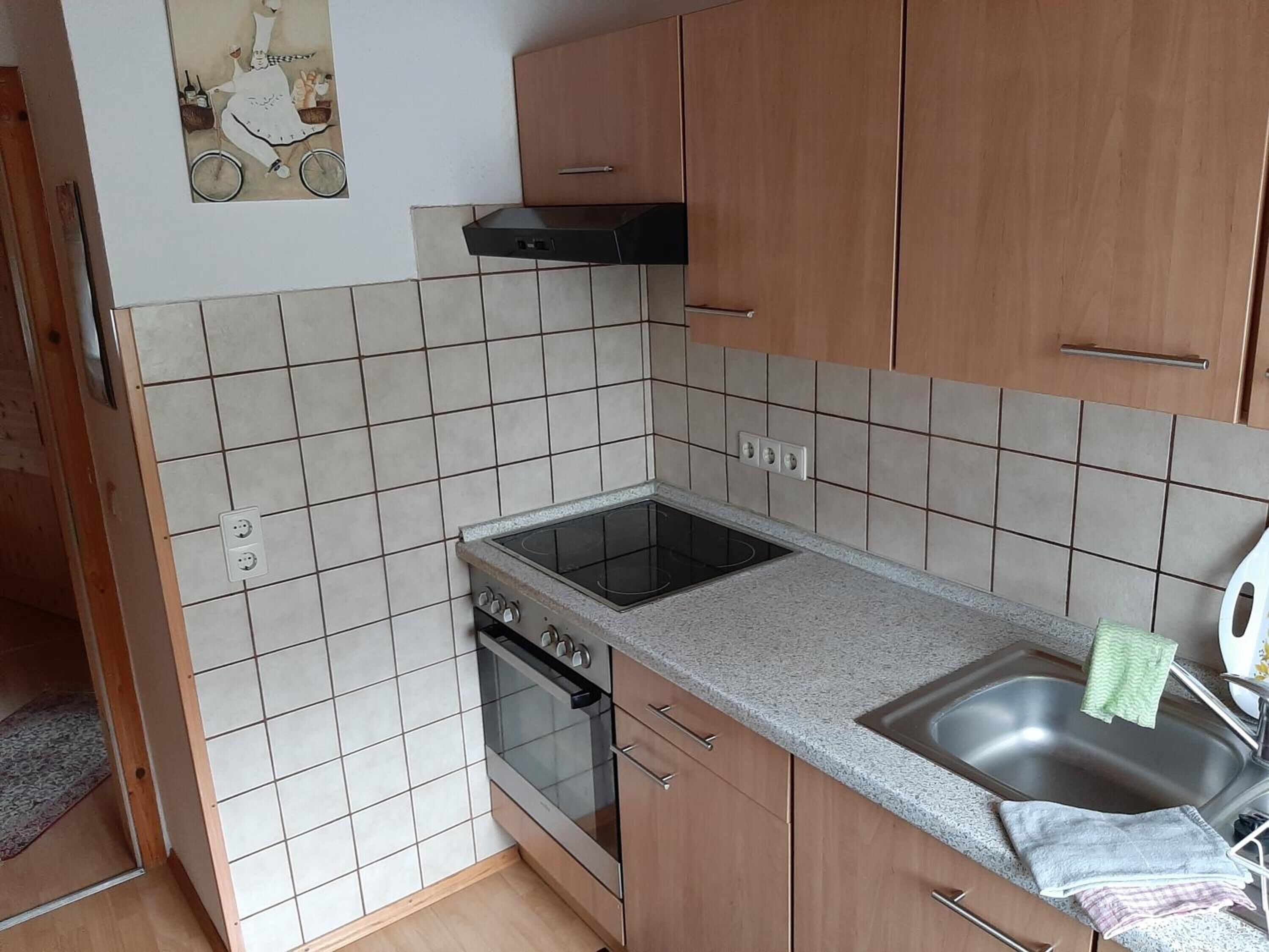 A compact kitchen with a stove, oven, and sink, wooden cabinets, and a tiled backsplash.